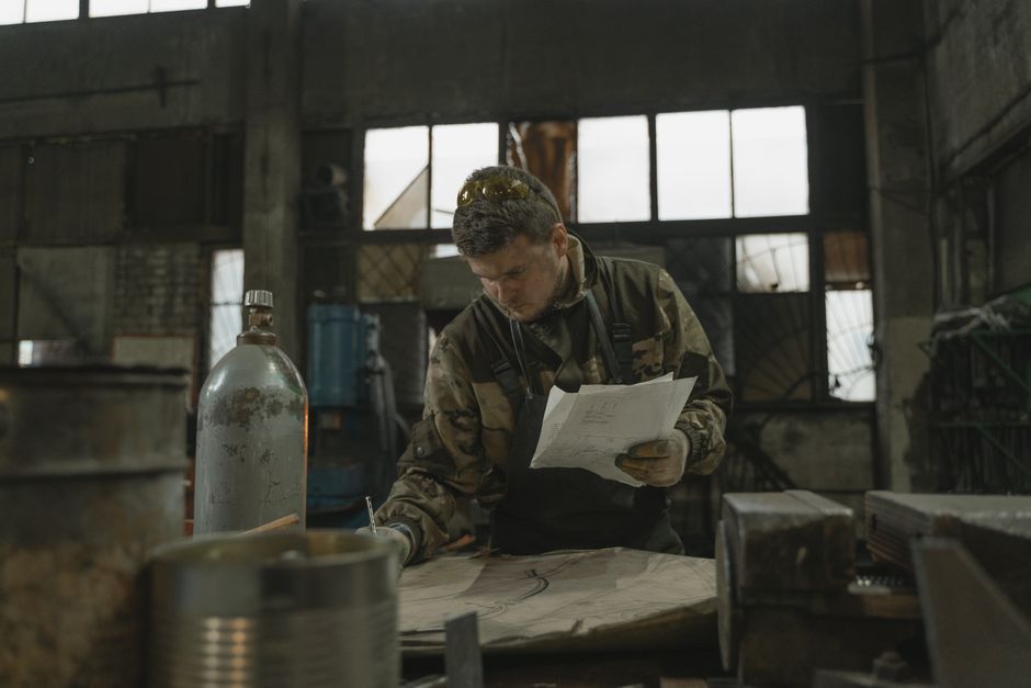 A blacksmith focused on drawing and metalwork inside a rustic workshop. (Photo: Tima Miroshnichenko / Pexels)