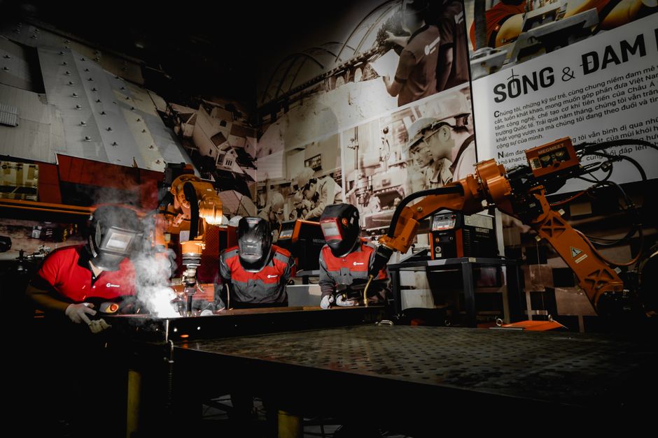 Three welders in protective gear working with robots in a high-tech industrial workshop. (Photo: Hoang NC / Pexels)