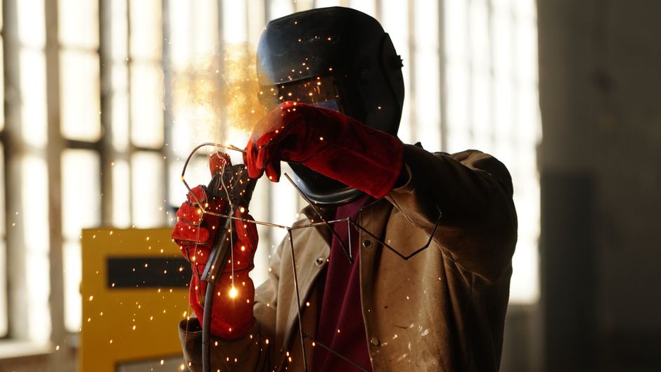 A welder working with sparks in a factory setting, showcasing safety gear and precision. (Photo: Aziz Er / Pexels)