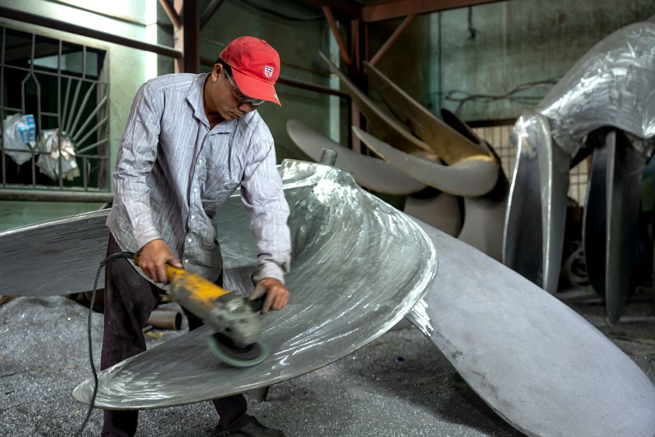Worker in a workshop grinding a large metal propeller, showcasing industrial craftsmanship. (Photo: Quang Nguyen Vinh / Pexels)