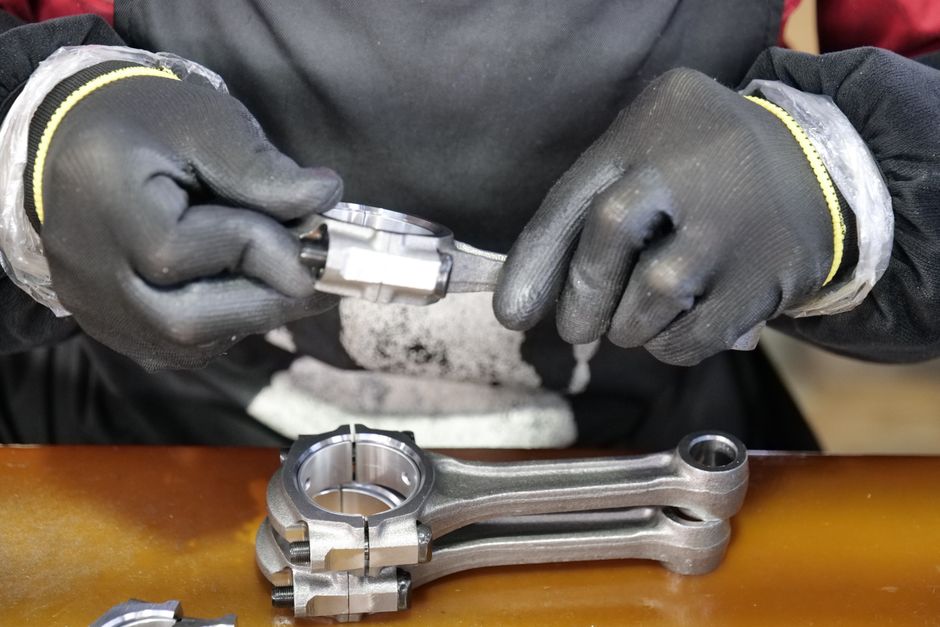 Close-up of a technician's hands assembling a metal connecting rod with precision and care. (Photo: Auto Tech / Pexels)