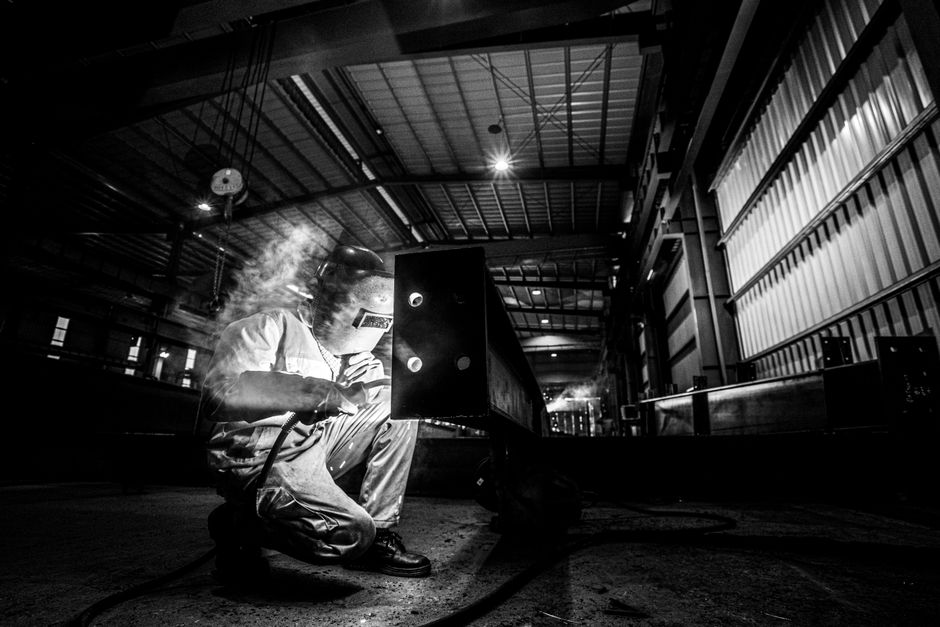 Monochrome image of a welder at work in an industrial factory setting. (Photo: Hoang NC / Pexels)