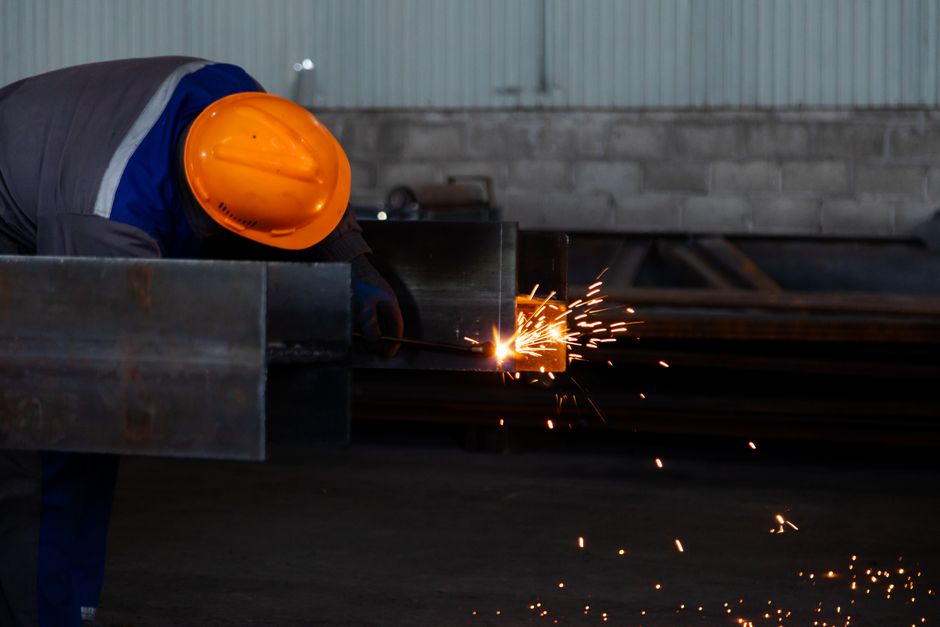 Worker wearing safety gear welds metal beam, emitting sparks in a factory setting. (Photo: Collab Media / Pexels)