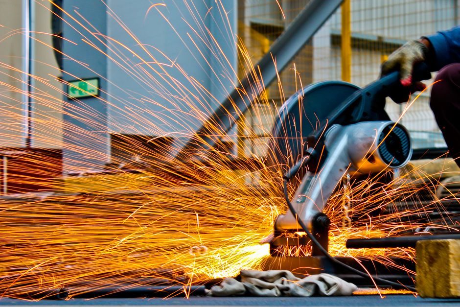 A worker operates a grinder cutting metal, creating a vibrant display of sparks in an industrial setting. (Photo: Anamul Rezwan / Pexels)