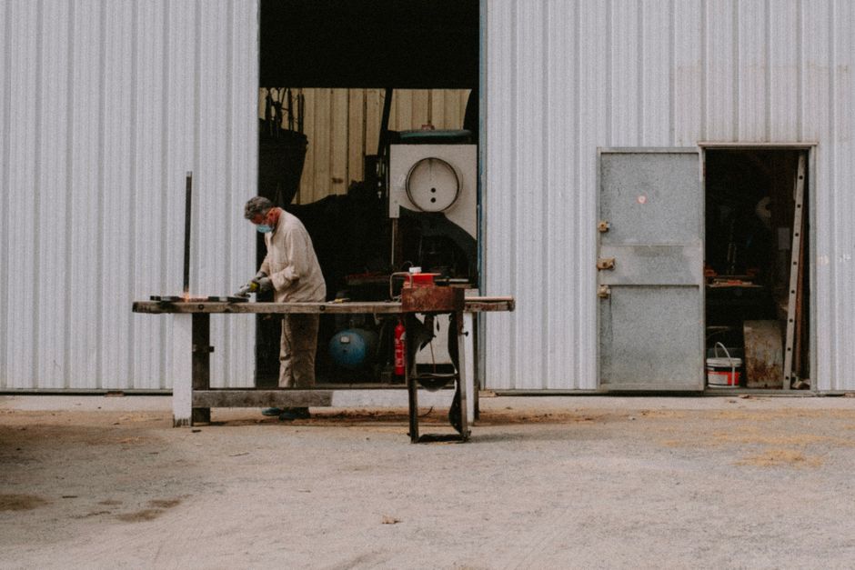 A metal worker using a grinder outside a large industrial warehouse. (Photo: Mathias Reding / Pexels)