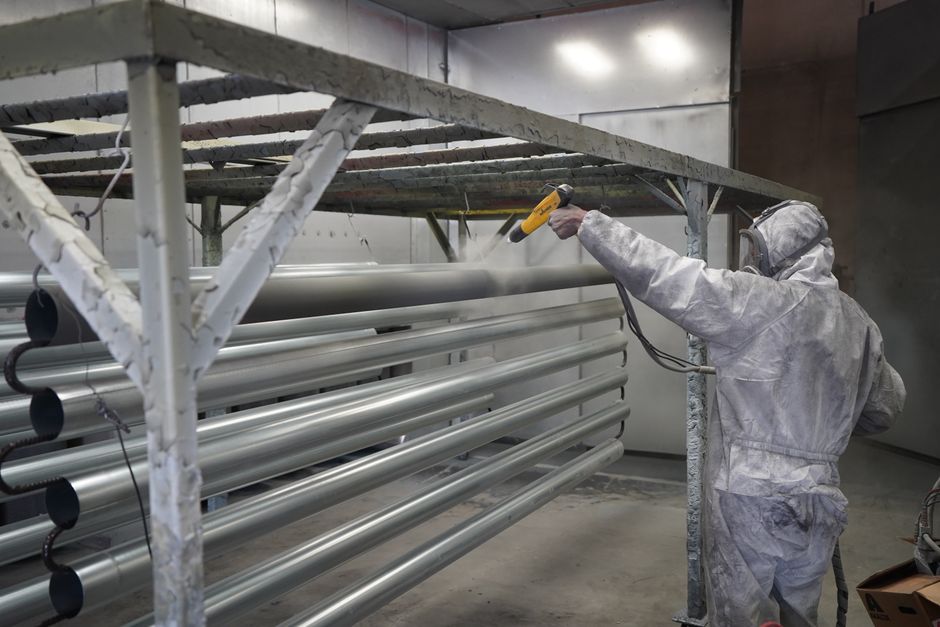 Worker in protective gear applying powder coating to metal pipes in a factory setting. (Photo: Full Blown Coatings https://www.fullblowncoatings.com/ / Pexels)