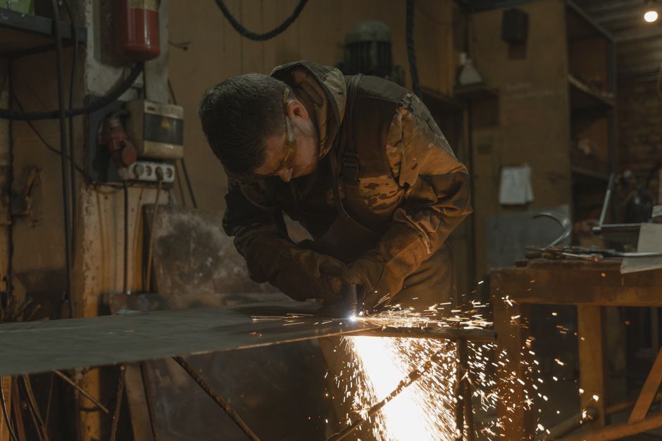 A focused welder in protective gear working with metal, creating vivid sparks in a workshop. (Photo: Tima Miroshnichenko / Pexels)