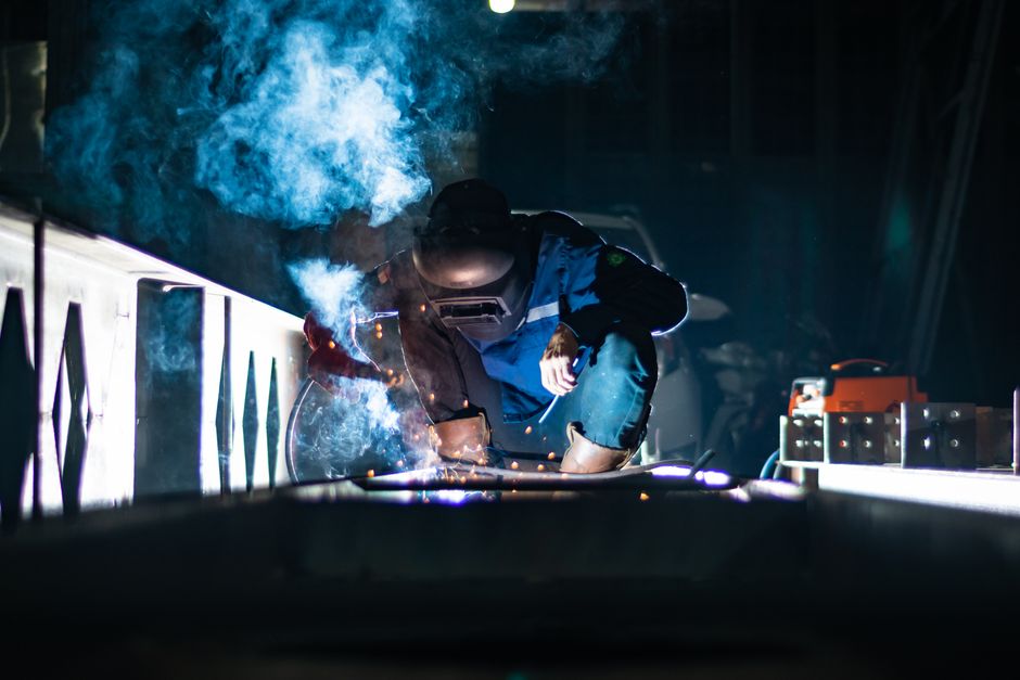 A welder working at night producing sparks and smoke in an industrial setting. (Photo: ERFIN EKARANA / Pexels)
