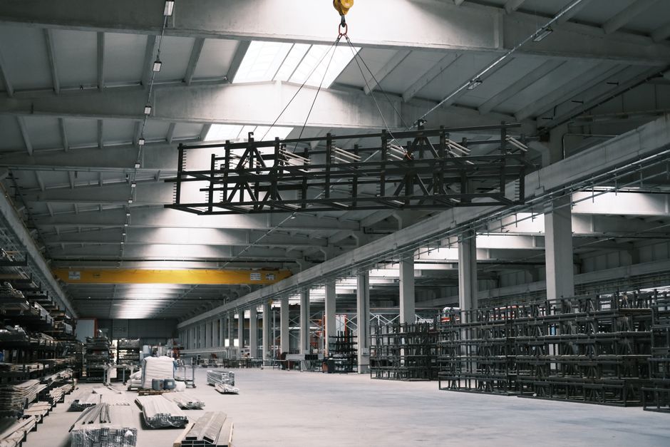 Spacious industrial warehouse interior with a yellow crane lifting metal framework. (Photo: Cemrecan Yurtman / Pexels)