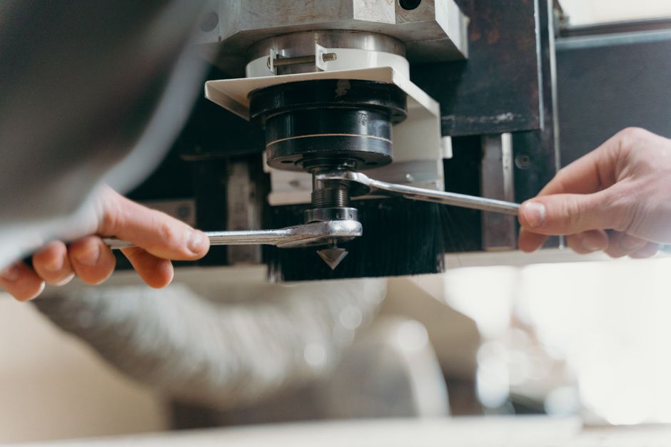 Close-up of hands adjusting a CNC machine using wrenches in an industrial setting. (Photo: cottonbro studio / Pexels)