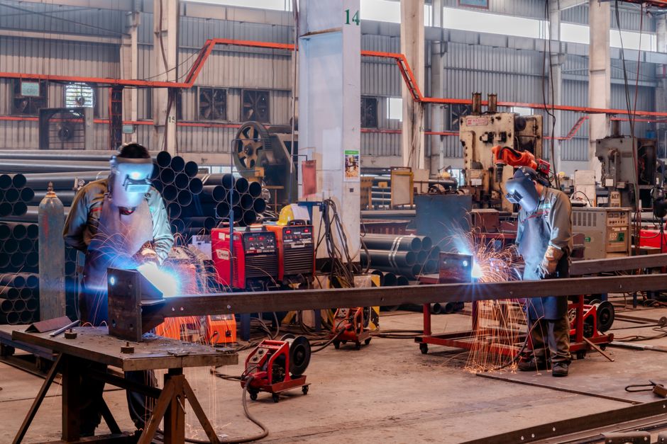 Two welders wearing protective gear working in a busy industrial factory workshop. (Photo: Hoang NC / Pexels)