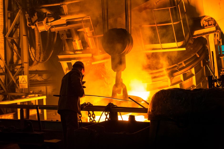 A worker operates machinery in a factory with molten metal and intense flames. (Photo: Kateryna Babaieva / Pexels)