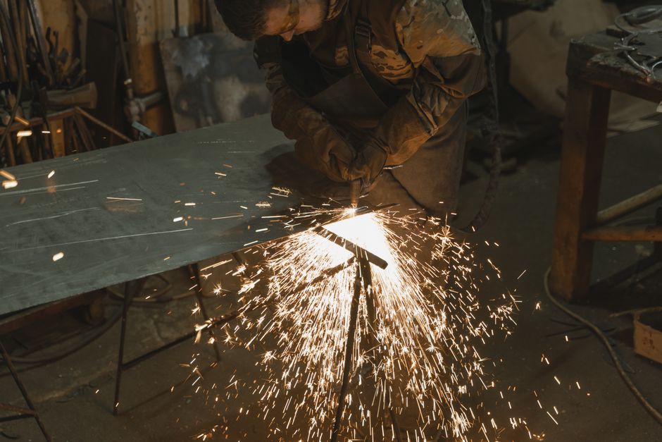 A professional welder cutting metal in an industrial workshop with bright sparks flying around. (Photo: Tima Miroshnichenko / Pexels)