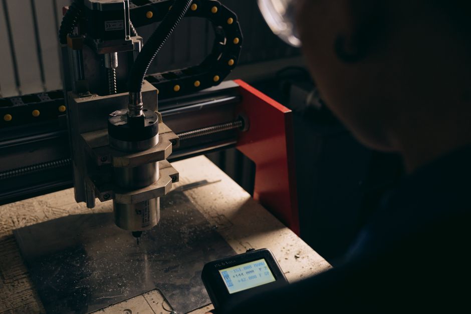 A detailed view of a CNC machine being operated by a person indoors with dim lighting. (Photo: Mikhail Nilov / Pexels)