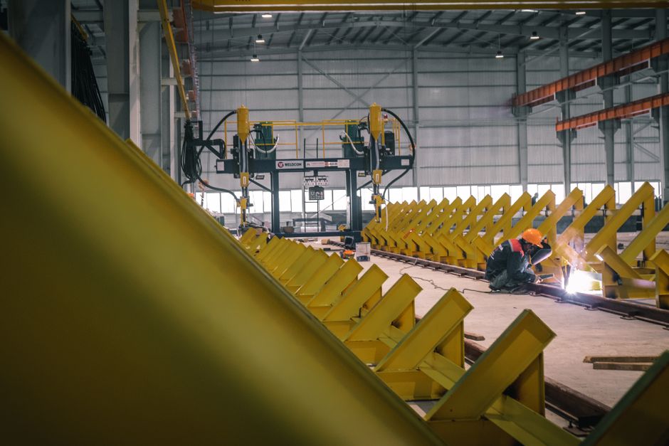 A worker welding metal in an industrial warehouse with heavy machinery. (Photo: Hoang NC / Pexels)