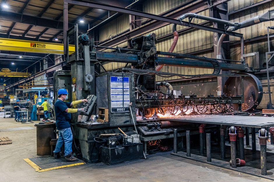 A worker wearing safety gear operates machinery in a busy manufacturing factory. (Photo: Rolled Alloys Specialty Metal Supplier / Pexels)