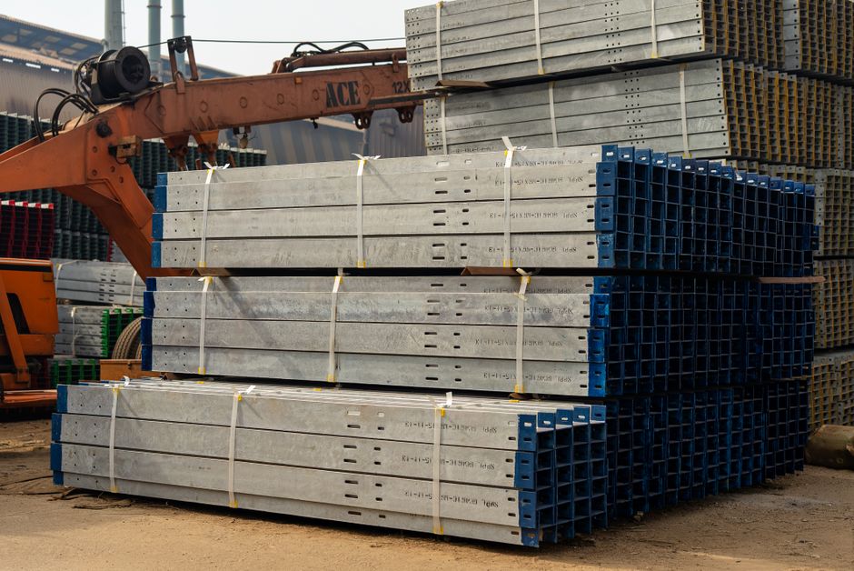 Stack of steel beams ready for construction in an industrial setting with crane. (Photo: Michael Orshan / Pexels)