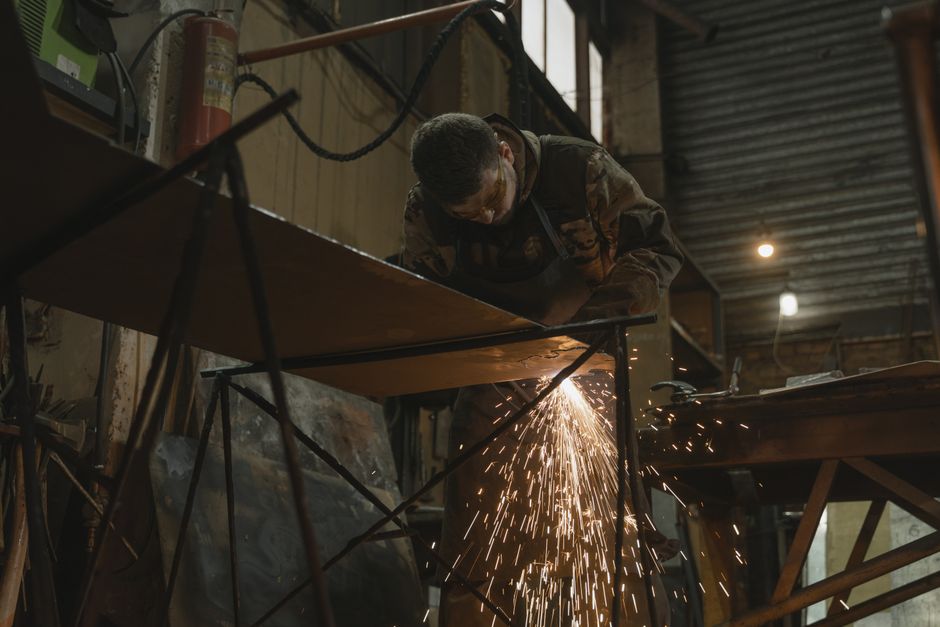 A worker focused on welding metal inside an industrial setting with sparks flying. (Photo: Tima Miroshnichenko / Pexels)