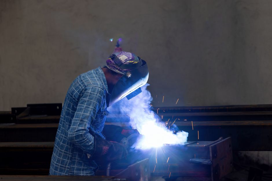 A welder in protective gear working with sparks in an industrial factory environment. (Photo: Mohan Nannapaneni / Pexels)